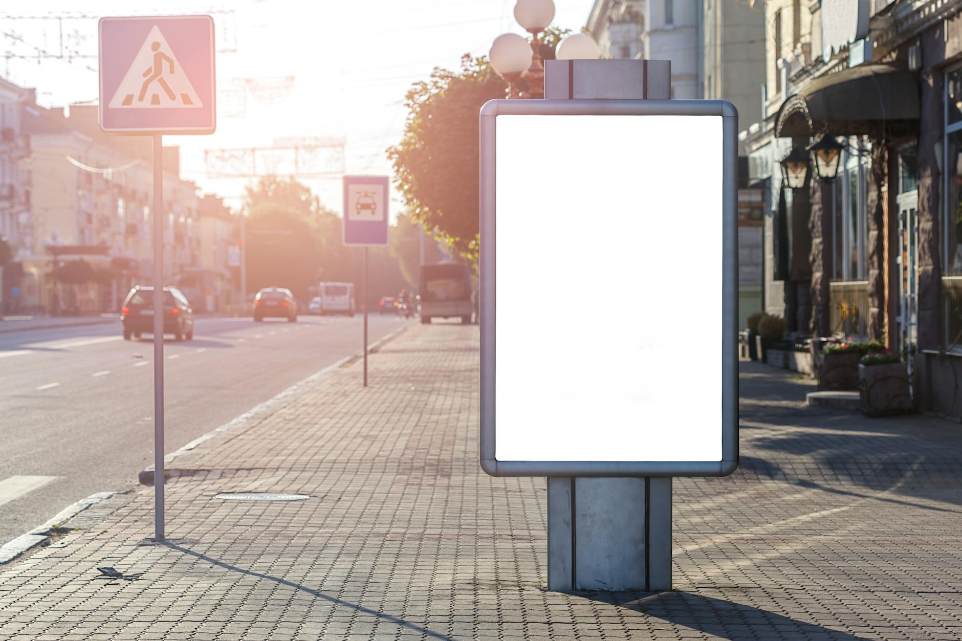 a blank vertical banner display panel standing on a paved city footpath beside a retail strip
