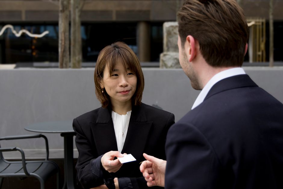 a businesswoman handing her printed business card to a client at an outdoor meeting