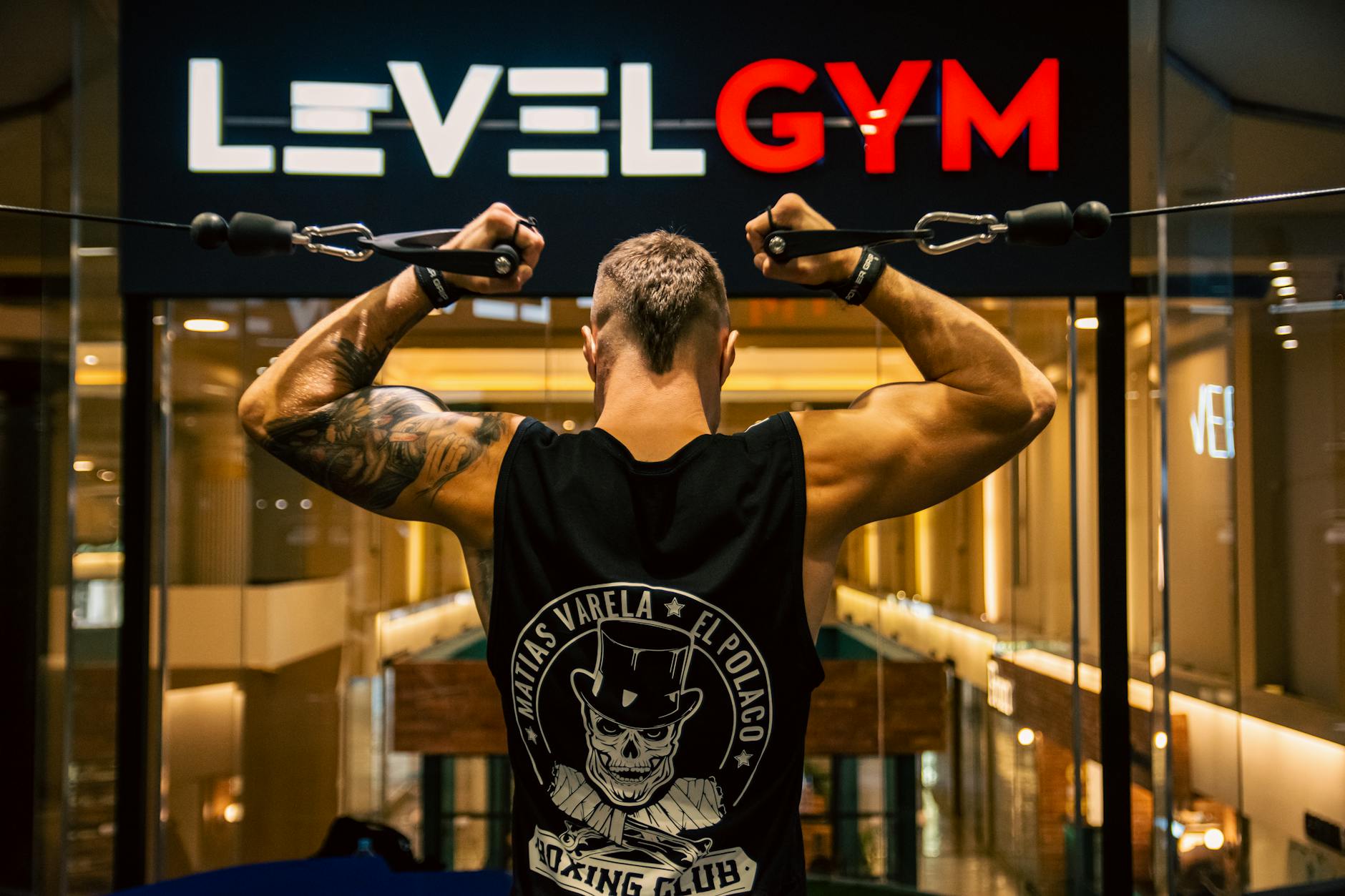 an athlete training on a cable machine beneath an illuminated gym brand sign