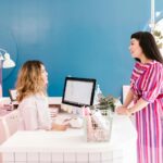 a modern Australian hair salon reception desk with a branded acrylic panel sign, a small stack of appointment cards in a card holder, and a