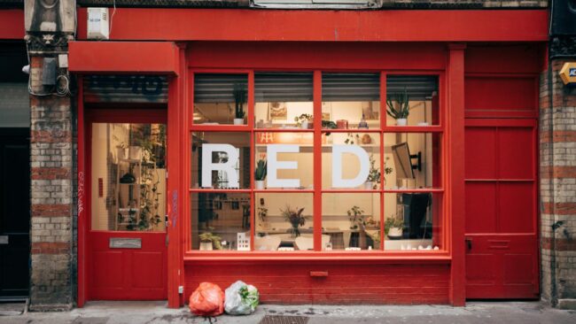 A retail shopfront window displaying bold red and yellow EOFY sale signage with percentage-off posters, A-frame sign on the footpath, and