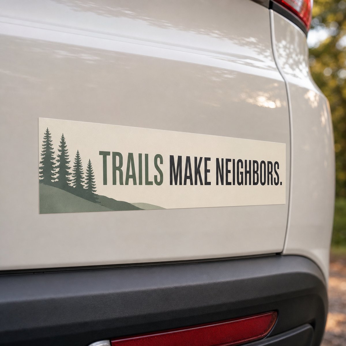 A weatherproof vinyl bumper sticker with a bold outdoor slogan and pine tree motif applied to the rear of a light coloured car