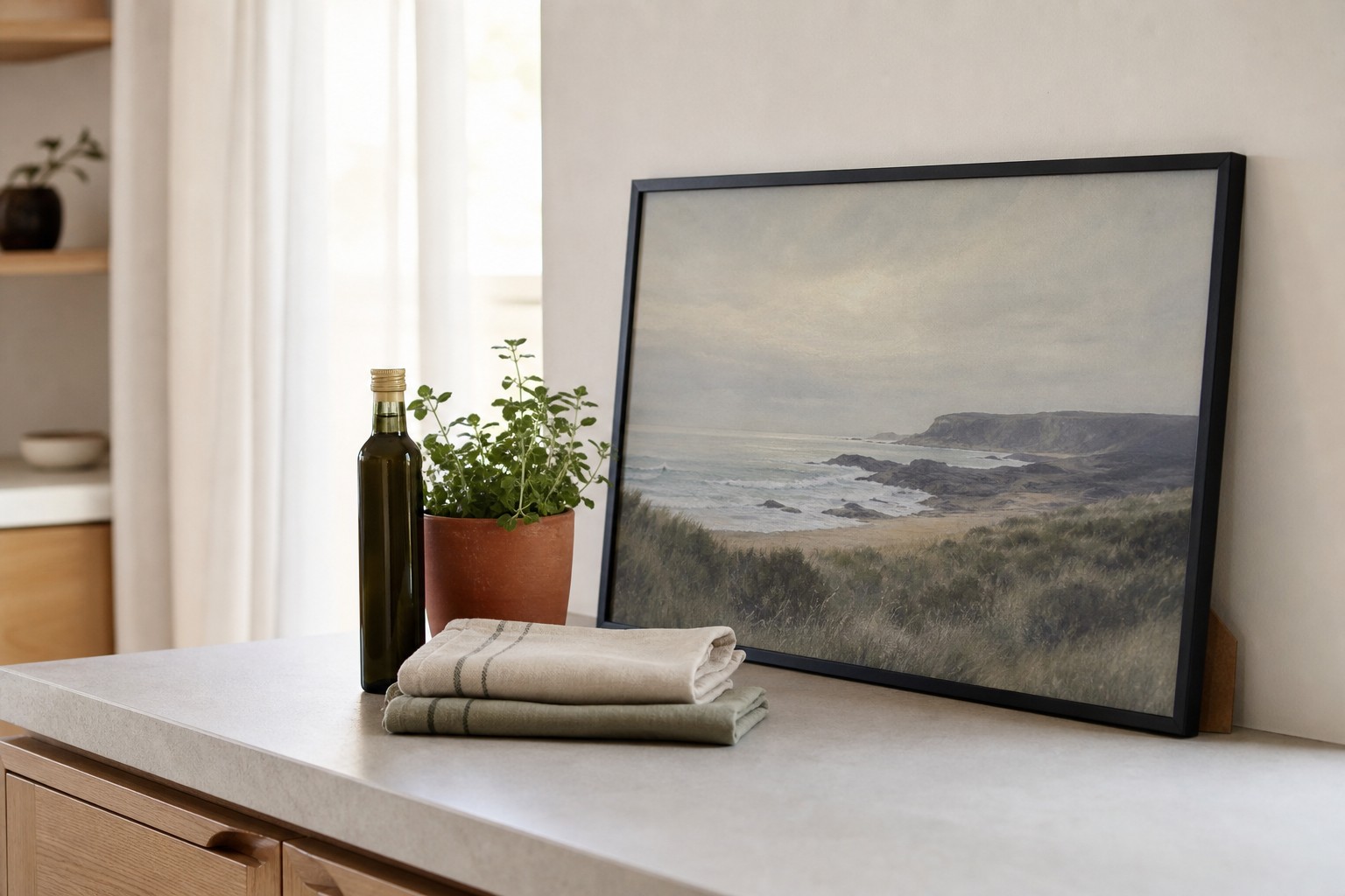 A3 black framed print leaning on a kitchen bench beside olive oil, a terracotta pot of herbs and folded linen tea towels