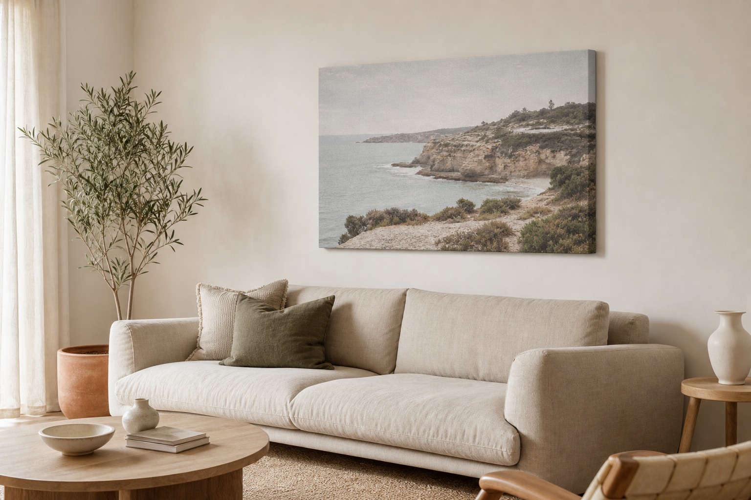 Large gallery wrap canvas print of a coastal landscape hanging above a low linen sofa in a bright living room