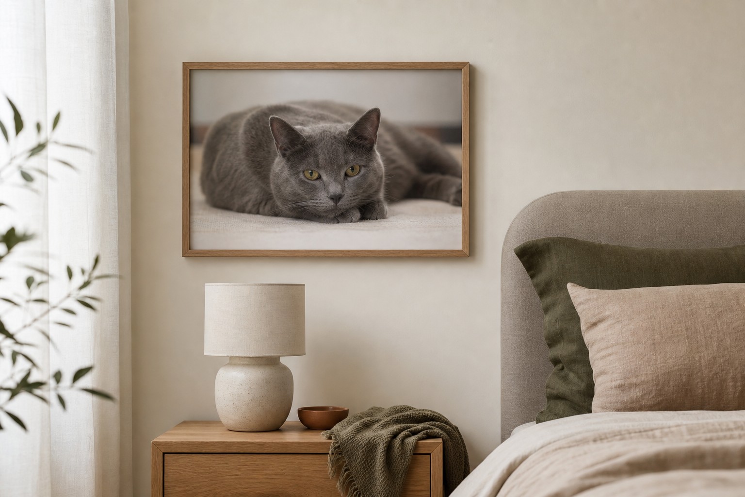 A3 natural oak framed print of a grey cat hanging on a bedroom wall above a bedside table