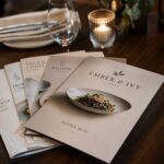 Stack of A4 restaurant menus with matte lamination fanned out on a dark timber dining table