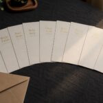 Nine cream certificates fanned across dark charcoal linen, gold titles catching low light, with a kraft envelope and a small potted plant nearby