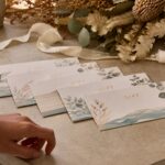 Several identical A6 gift vouchers with short gold foil titles overlapping on a boutique counter styled for an Australian summer Christmas.