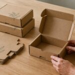 Kraft mailer boxes stacked on timber with hands opening one, clearly showing the RETF tuck-front closure mechanism.