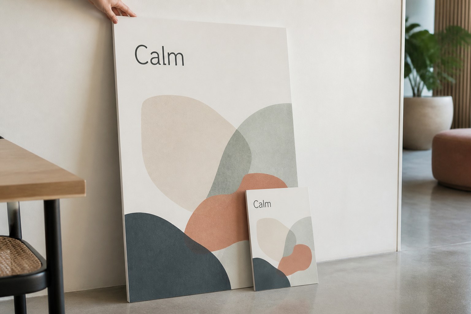 Large and small printed foam boards lean against a pale wall showing sand, terracotta, sage and deep blue layered curves, hand on the larger board.