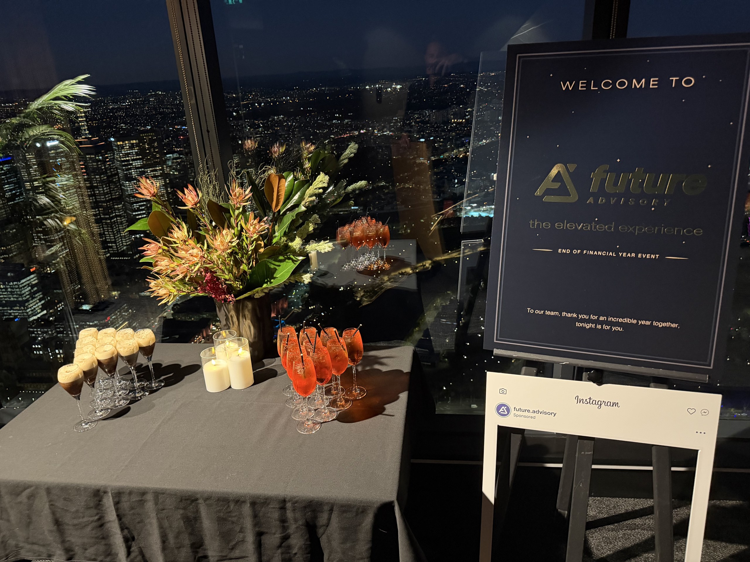 Styled event table with florals, candles and drinks beside the printed Future Advisory welcome sign and selfie frame