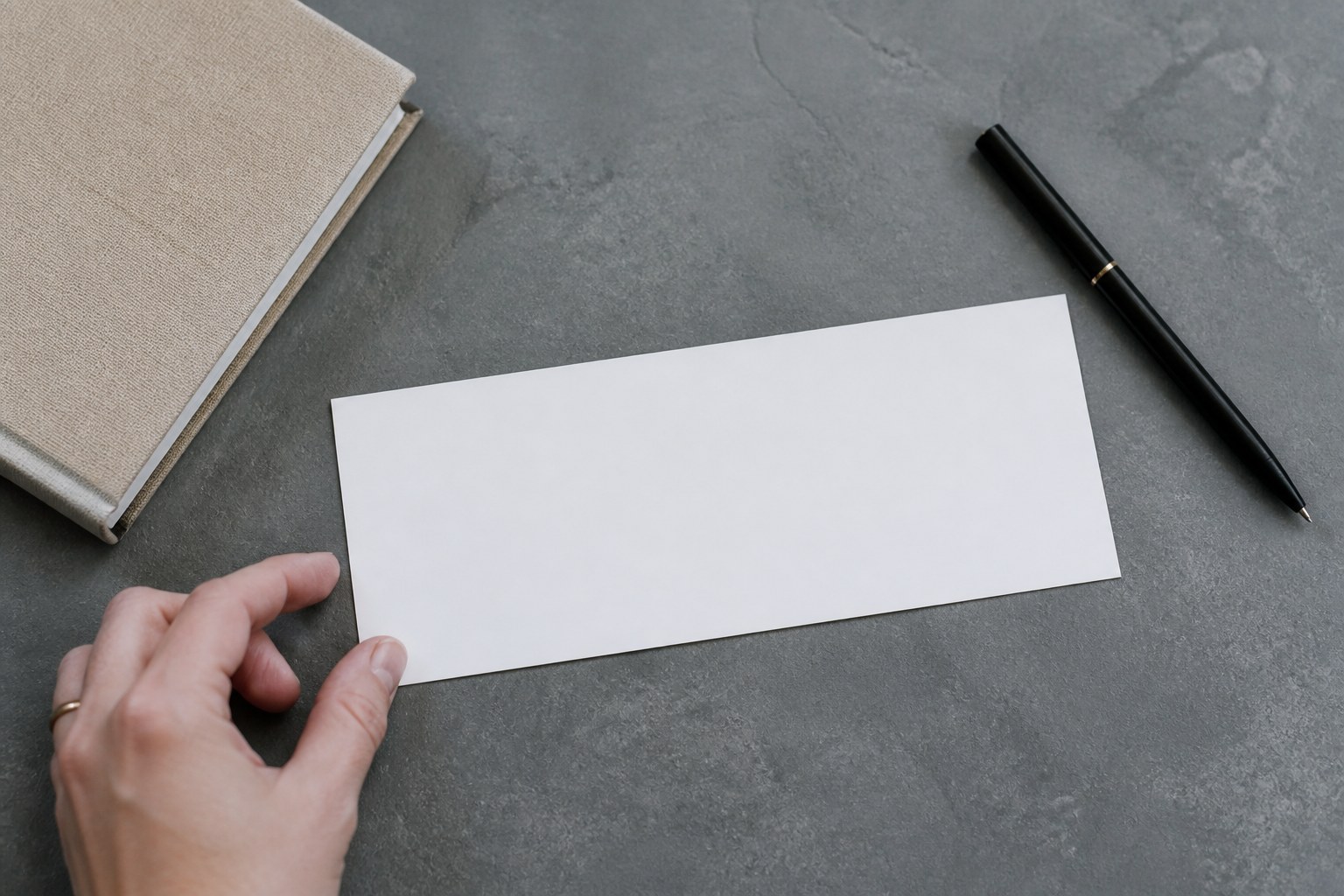Single DL gift voucher lying face down on a slate grey desk, blank back panel filling the frame, beside black pen and closed notebook.