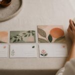Three postcards in ascending sizes lie fanned on linen, showing colourful front artwork above their blank address sides.