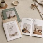 Several A4 booklets with saddle stitching spread on pale linen, sage, oat and white covers, one open to interior photos