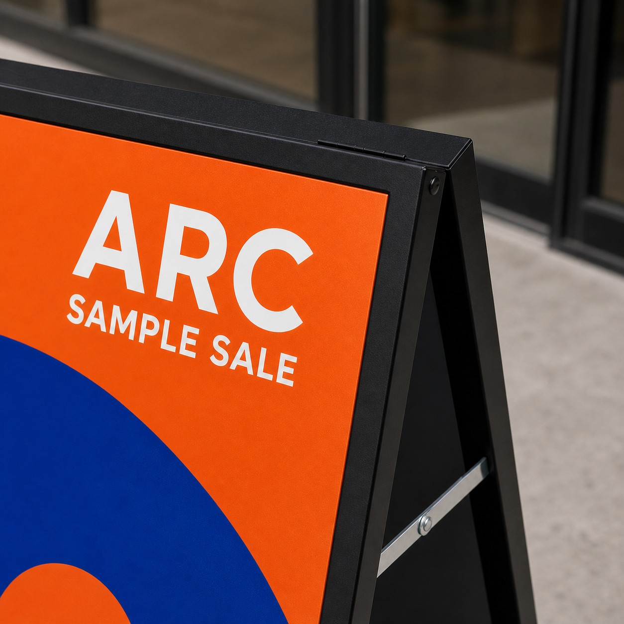 A-frame sign corner close up with laminated panel reflections, orange and blue print, black frame, top hinge and blurred shopfront behind