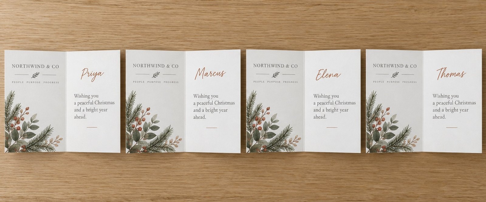 Four identical open A6 cards in a row on pale oak desk, recipient names in terracotta script differ at top of each right leaf