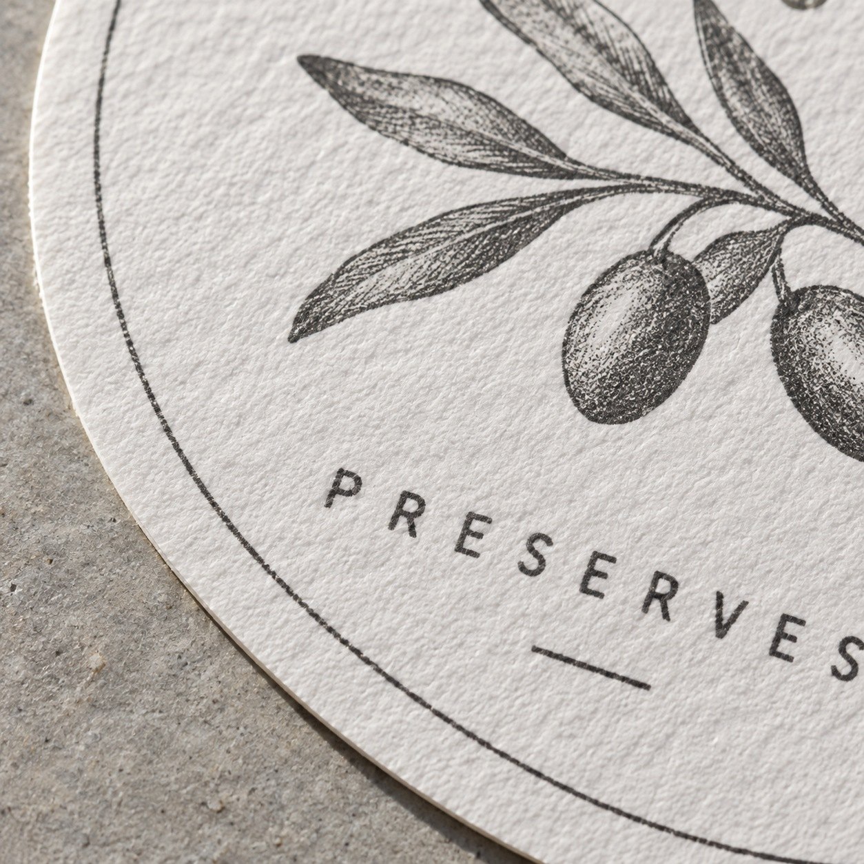 Bright white felt sticker in extreme close up with soft dimpled texture, part of a charcoal sprig and matte small capitals