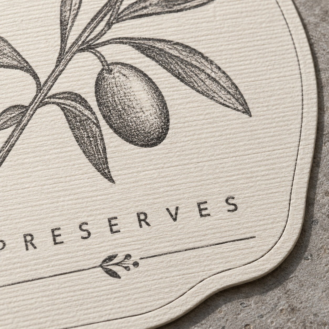 Extreme close up of warm cream linen sticker with fine parallel ribs, charcoal sprig and small spaced capitals