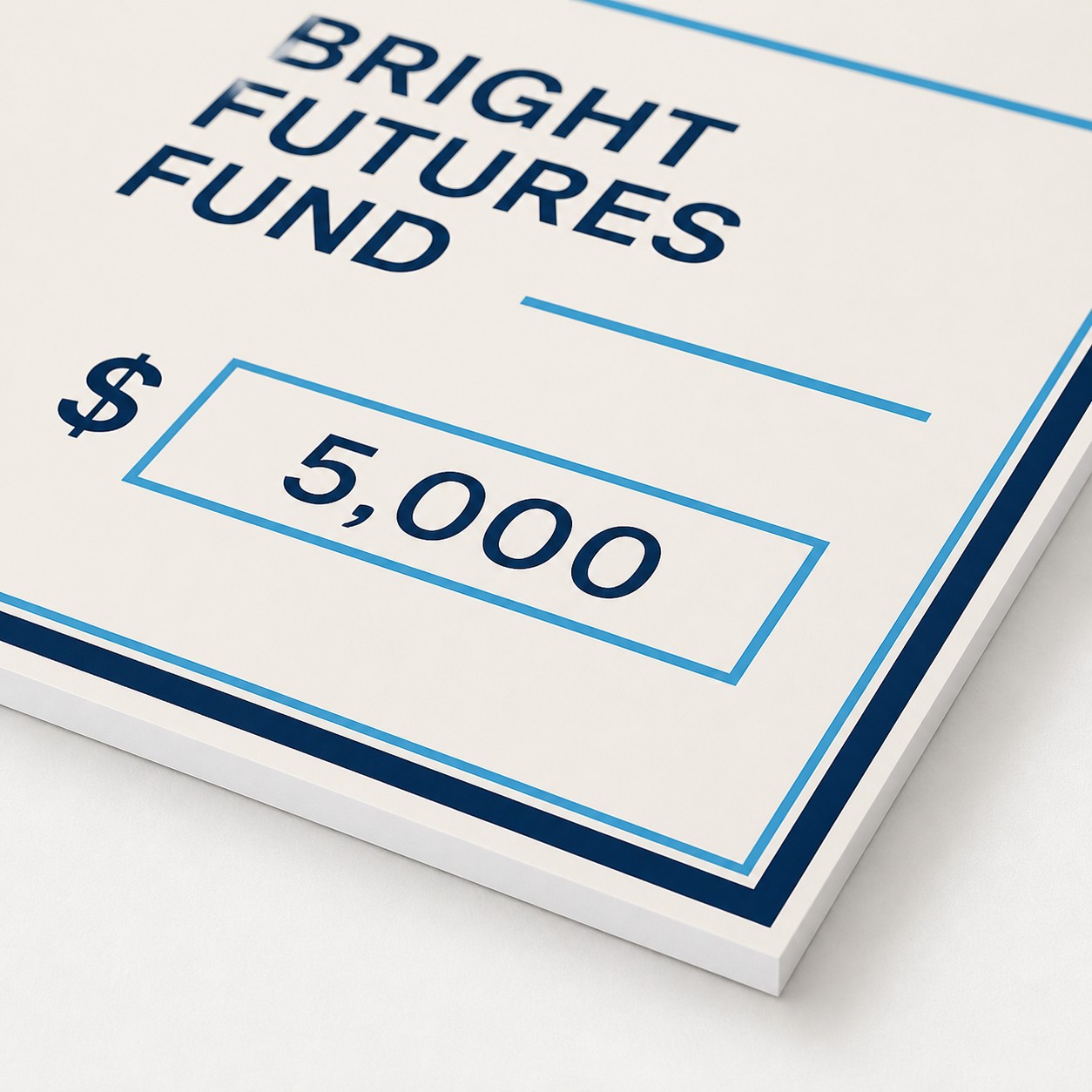 Novelty cheque close up at an angle with dark blue and light blue print on cream matte board, ruled lines, boxes and visible edge thickness.