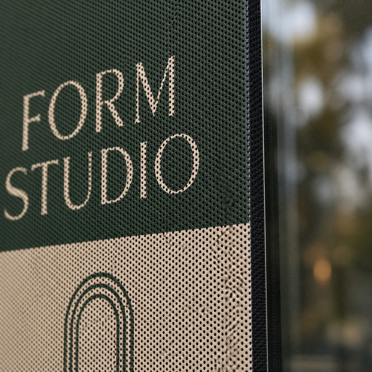 One way window film close up on glass showing forest green and cream print with individual perforations and blurred street scene behind.
