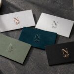 Five business cards fanned on charcoal slate with sprig monograms in terracotta ink, silver, raised clear gloss, tone on tone gloss and copper foil.