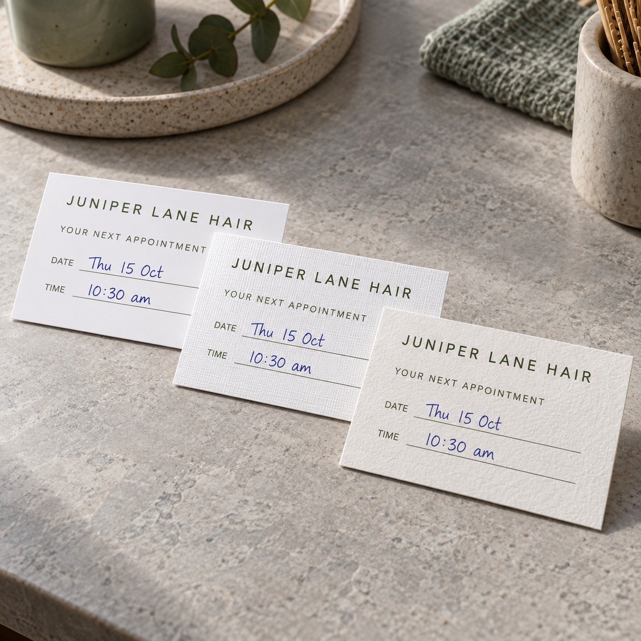 Three appointment card samples overlapping on grey stone, on smooth matte, linen textured and off white cotton paper