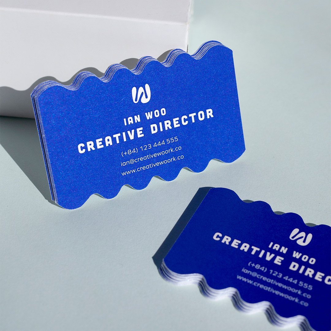 Deep blue business cards with a wavy cut edge and white lettering, one stack standing upright and another lying flat on a pale surface.