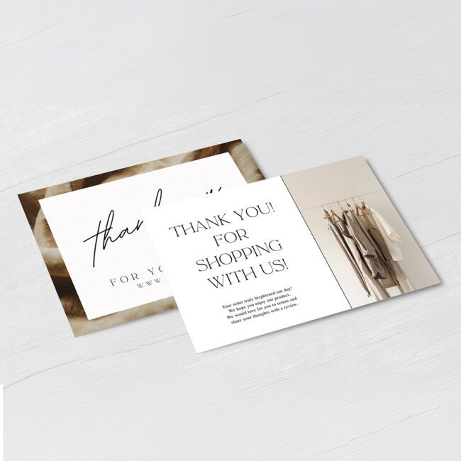Two postcards on a pale gray wood surface, one with large script and one reading thank you for shopping with us beside a small clothes rail photo.