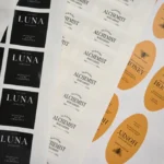 Overlapping sticker sheets: black labels with white lettering, white labels with dark lettering, and orange oval labels with a bee illustration.