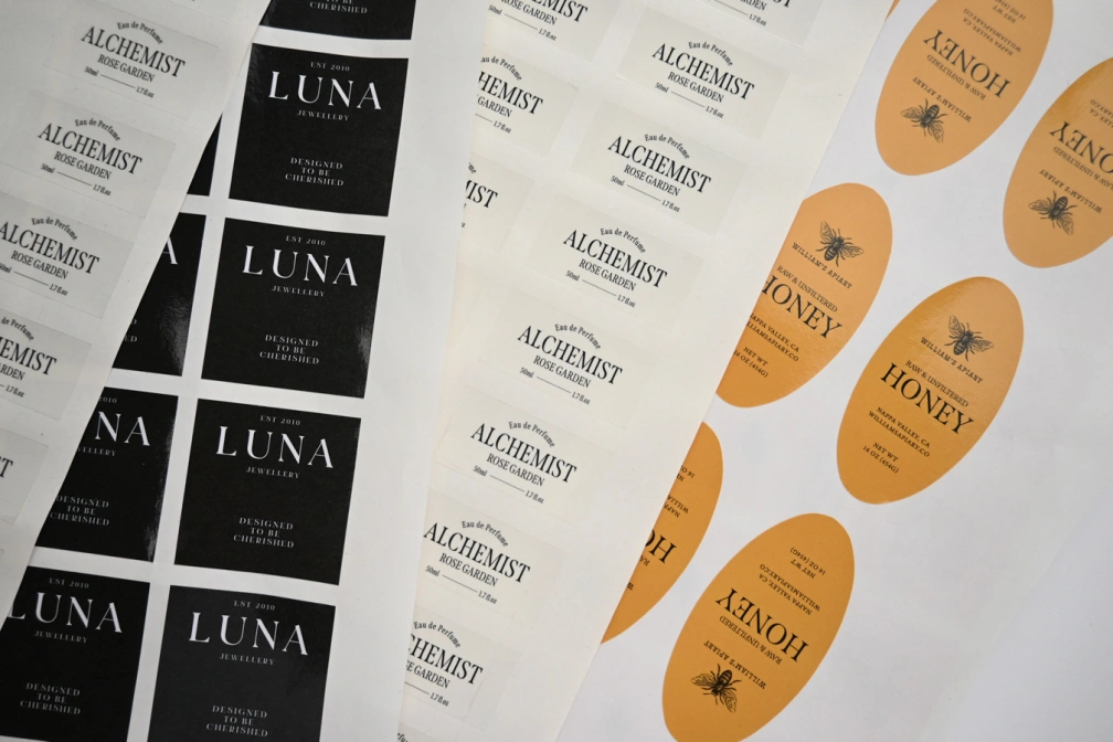 Overlapping sticker sheets: black labels with white lettering, white labels with dark lettering, and orange oval labels with a bee illustration.