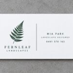 A bright white 100% recycled EcoStar business card printed with a green fern logo, lying on grey concrete
