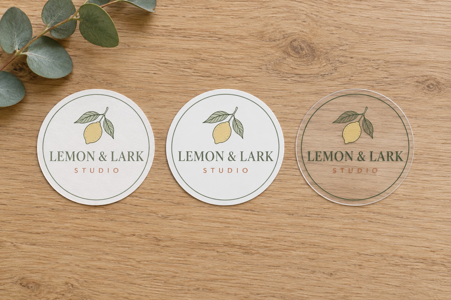 Illustration of the same round printed sticker three times side by side on a wooden table, on white matte paper, white matte vinyl, and clear vinyl