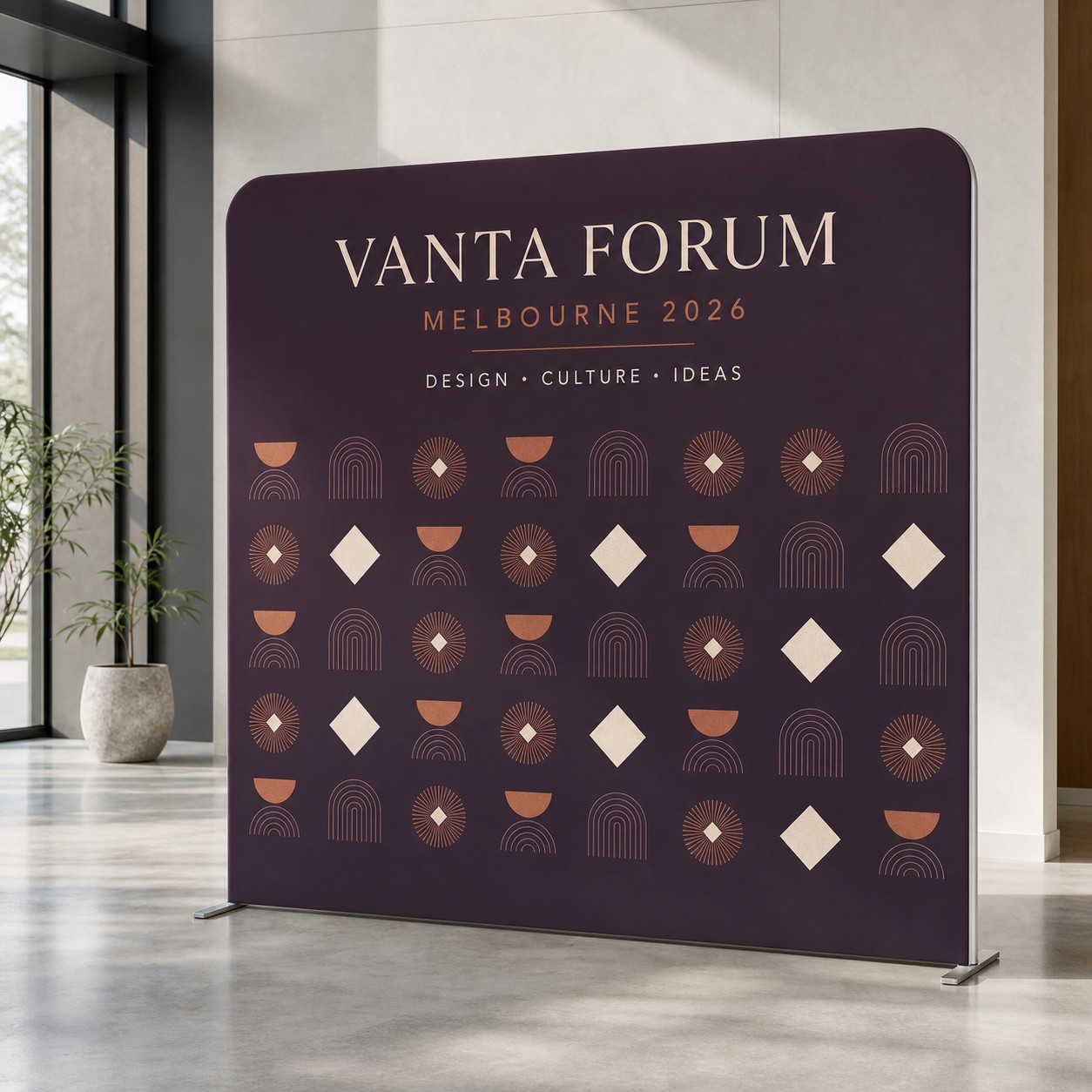 Stretch fabric media wall with plum, white and orange print on tension fabric over a tubular frame in a modern interior with white pillars.