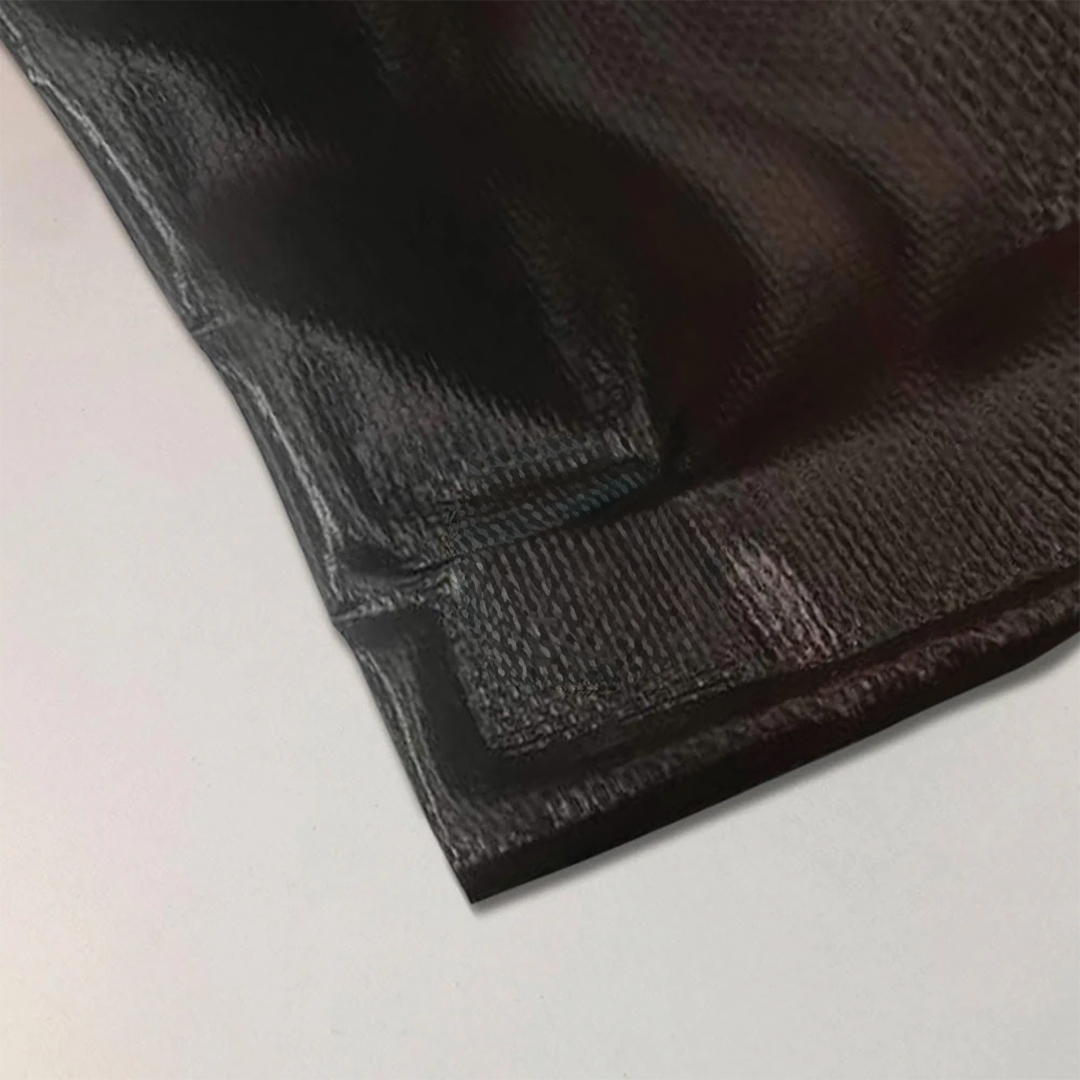 Dark vinyl banner corner lying on a pale grey surface, showing folded and welded hems along both edges and a visible woven texture.
