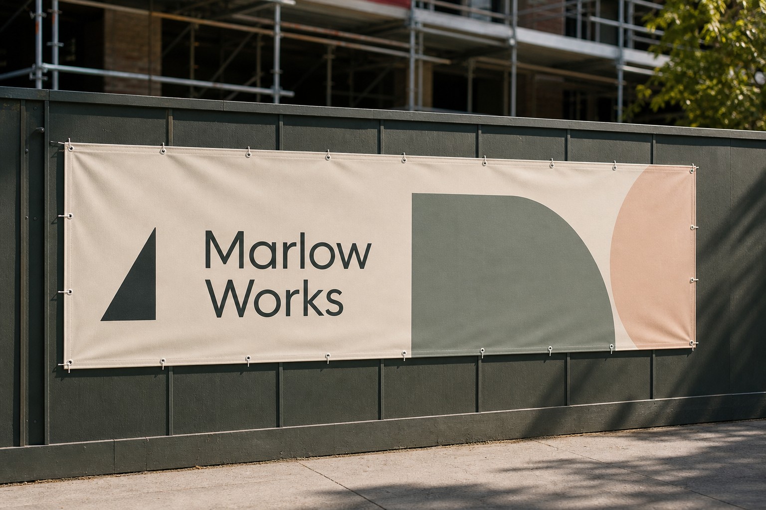 Long narrow printed vinyl banner across a dark green hoarding fence beside a footpath, with cream, sage and peach artwork and round eyelets.