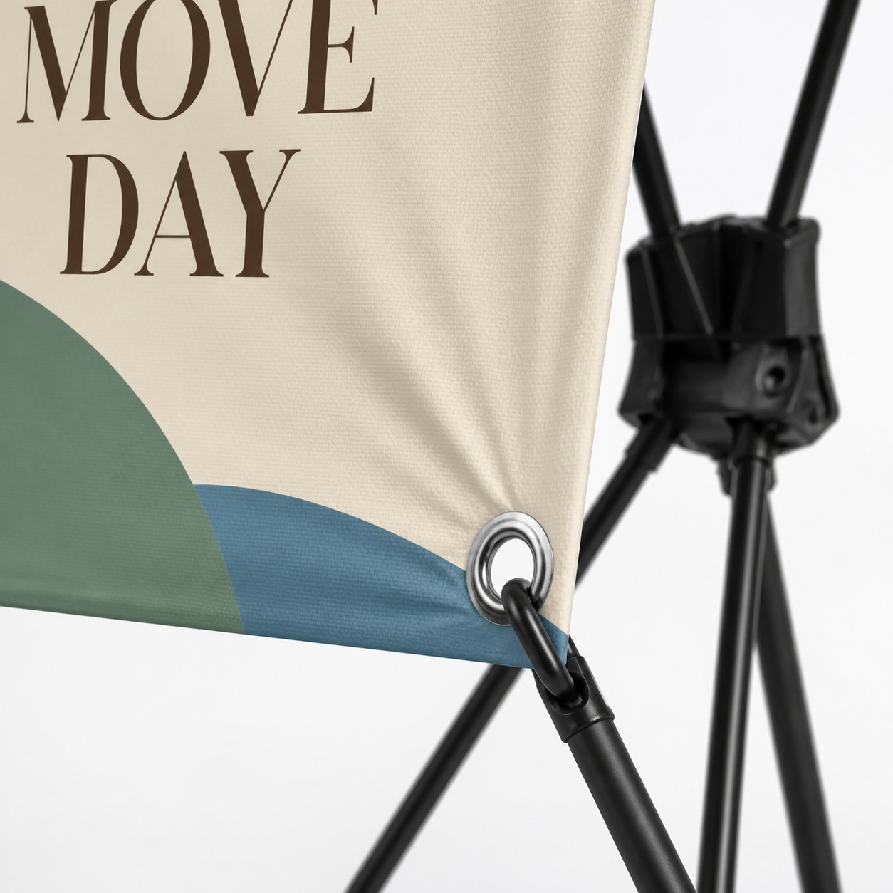 X banner stand corner close up with cream, dark green and blue print, silver grommet hooked to the black frame pole and fabric texture