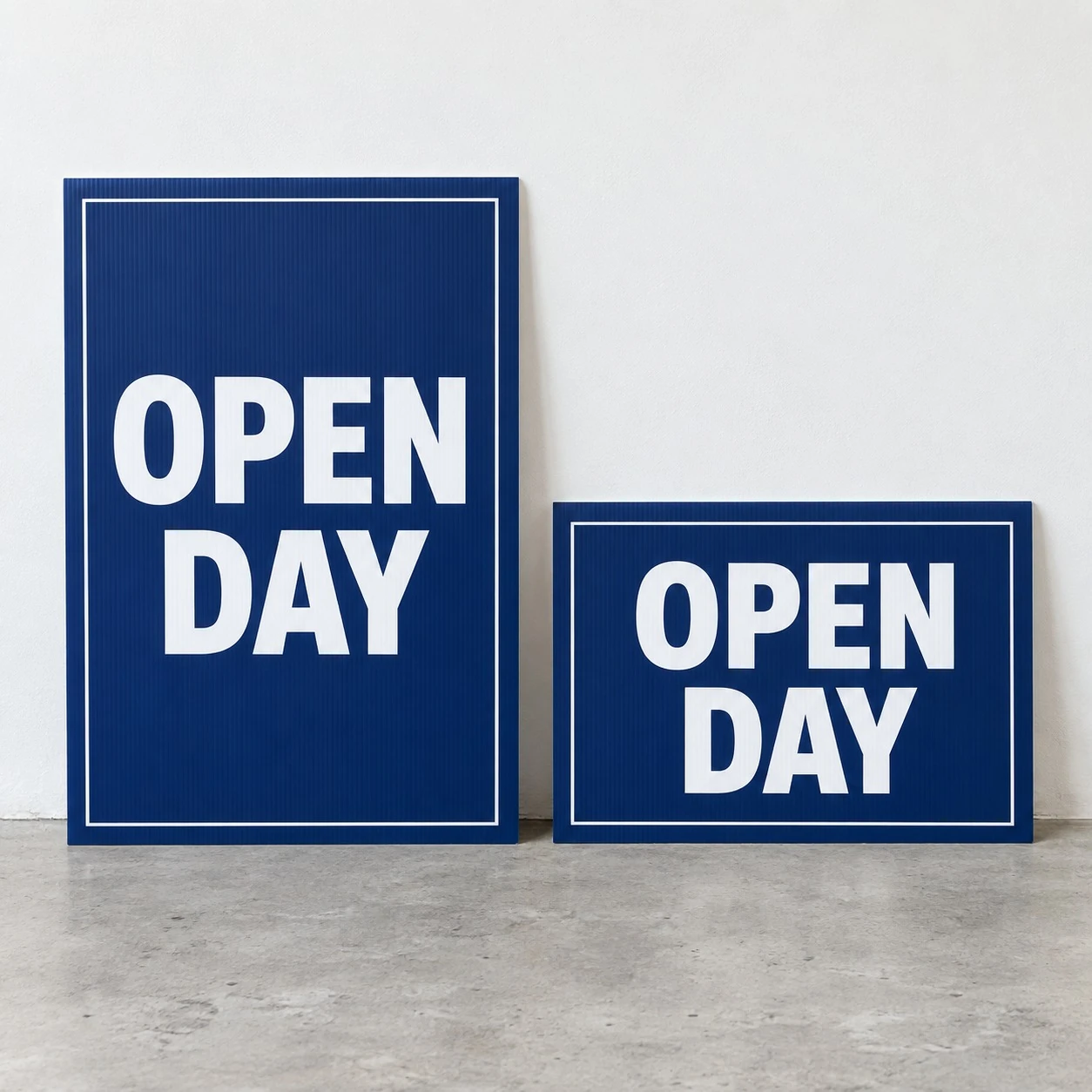 Two navy blue corflute signs with thin white borders and large white capitals stand side by side on a pale concrete floor.