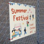 A cream corflute sign tied to a chainmesh fence through corner eyelets, with orange hand lettering, bunting and market illustrations.