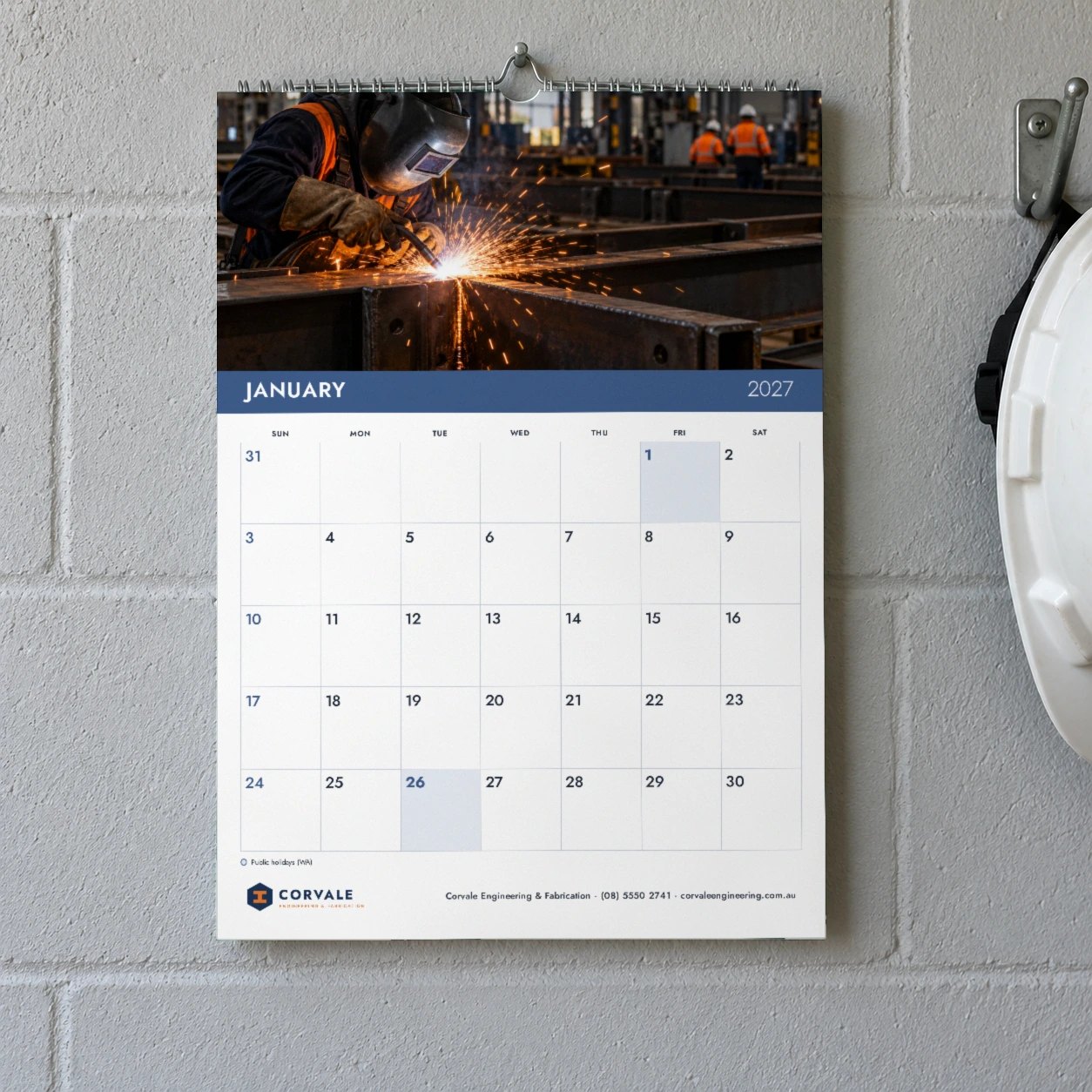 Planner layout 2027 wall calendar on grey block wall, welding photo with sparks above navy January band and large day boxes