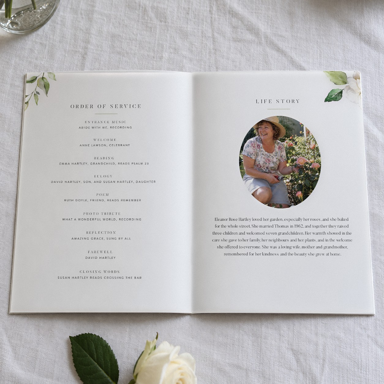 The White Garden booklet is open at pages 2 and 3 on white linen, with a round photo of a woman in a sun hat among roses and white roses in the top corners