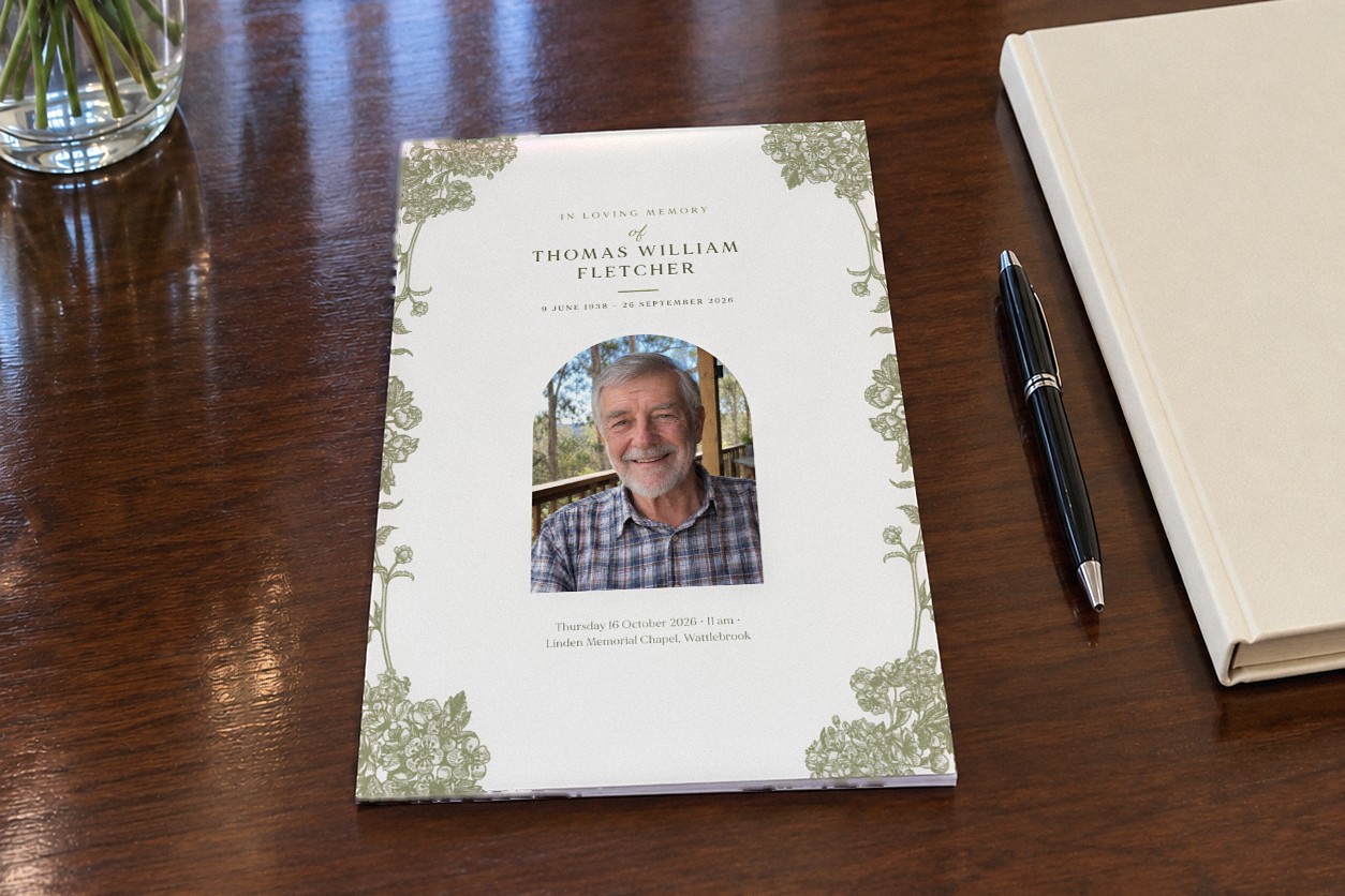Closed A5 funeral order of service booklet in the Visco Garden design on a dark polished timber table with olive green botanical flowers framing an arch shaped portrait of a smiling older man