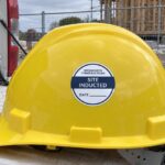 Yellow hard hat with a round navy and white Site inducted hard hat sticker resting on a white ute tailgate at a building site