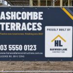 A navy mesh construction fence banner cable tied across a temporary fence panel in front of timber scaffolding