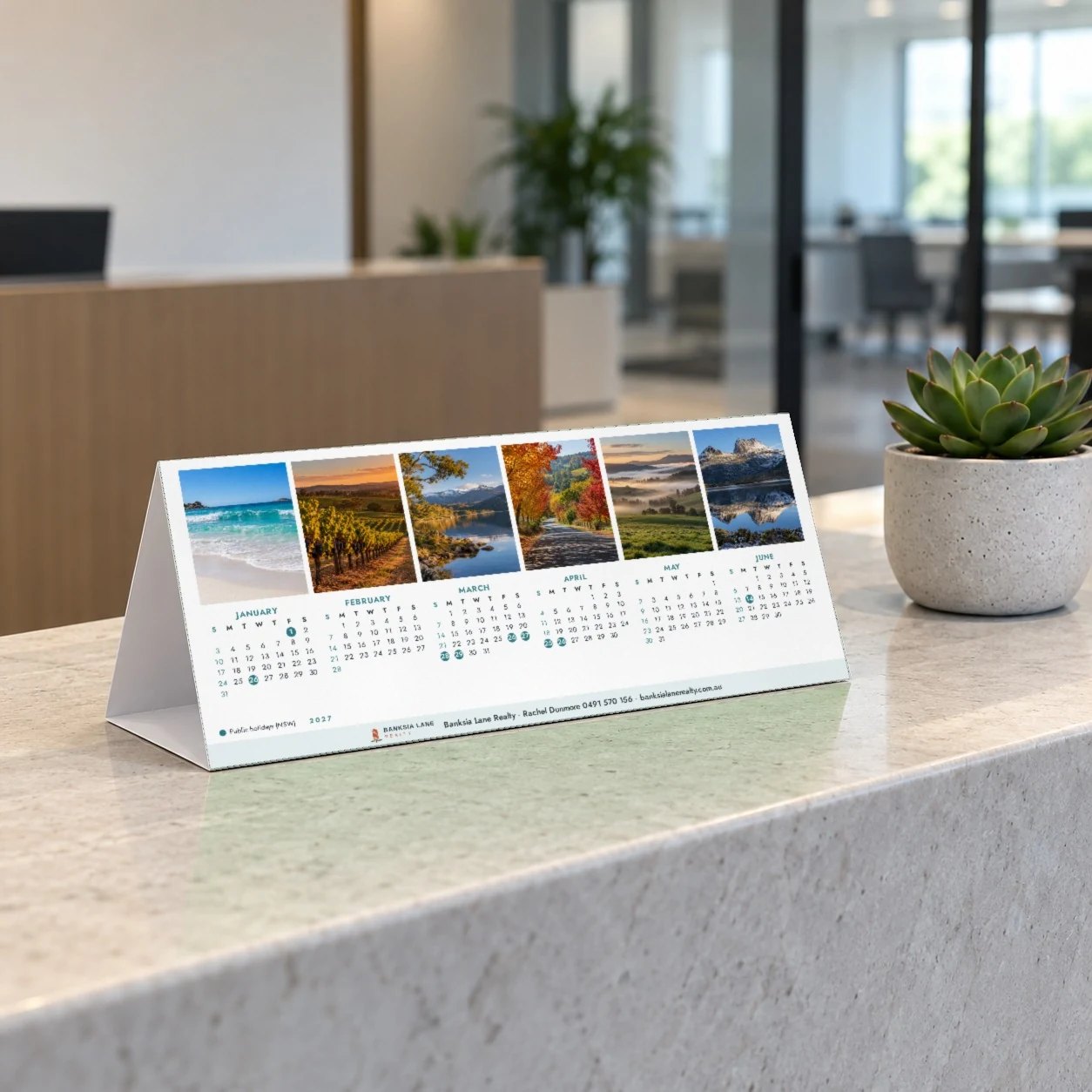 2027 tent desk calendar with six landscape photos above January to June on stone reception counter beside a succulent