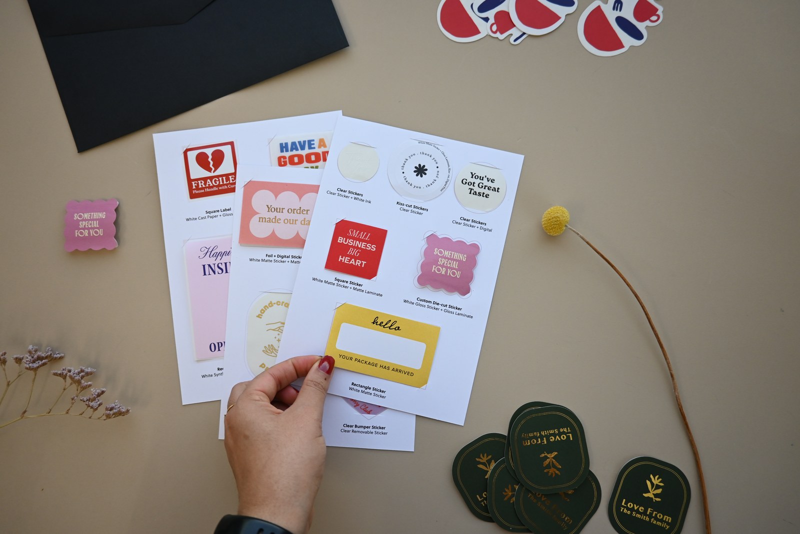 Hand holding white sample sheets over a beige surface · Sticker and Label Sample Pack · fixed contents, no artwork needed, try stocks before ordering